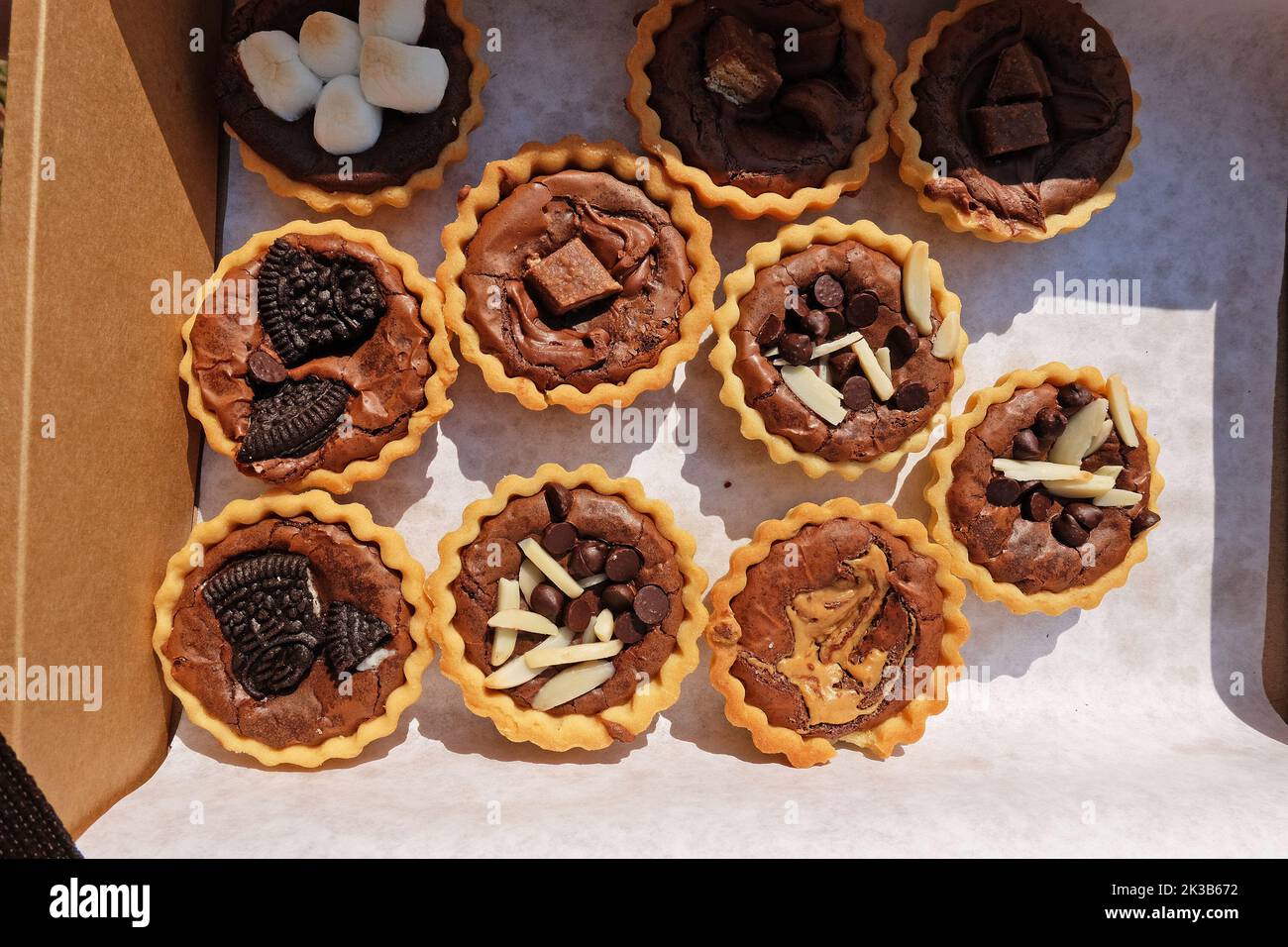 Primo piano scatola di carta di crostate di brownie al cioccolato fondente con fette di bastoncini di mandorle, marshmallow, bar di zucchero e burro di arachidi Foto Stock