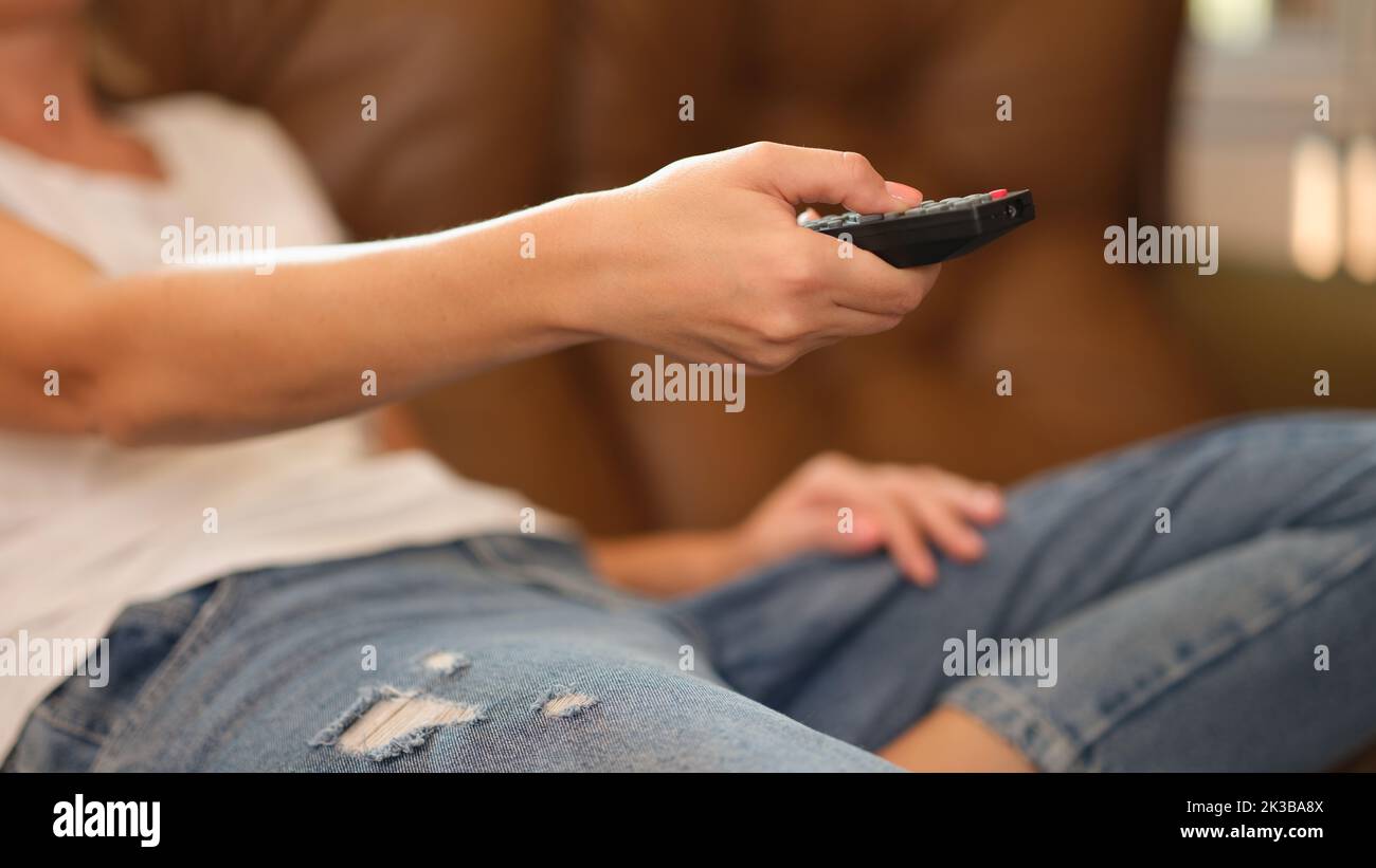 Donna con telecomando che guarda la TV a casa sdraiata sul divano Foto Stock