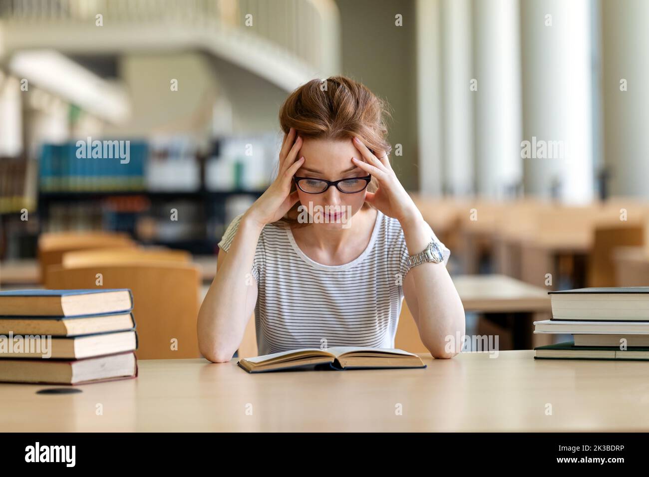Giovane donna esausta che studia e si prepara all'esame in biblioteca universitaria. Concetto di formazione Foto Stock