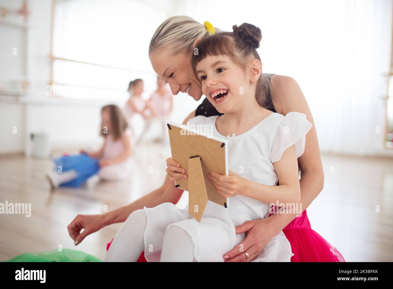 Felice ragazza disabile coccole con la madre e guardando la foto durante la lezione di balletto. Concetto di integrazione dei bambini disabili e della paternità. Foto Stock