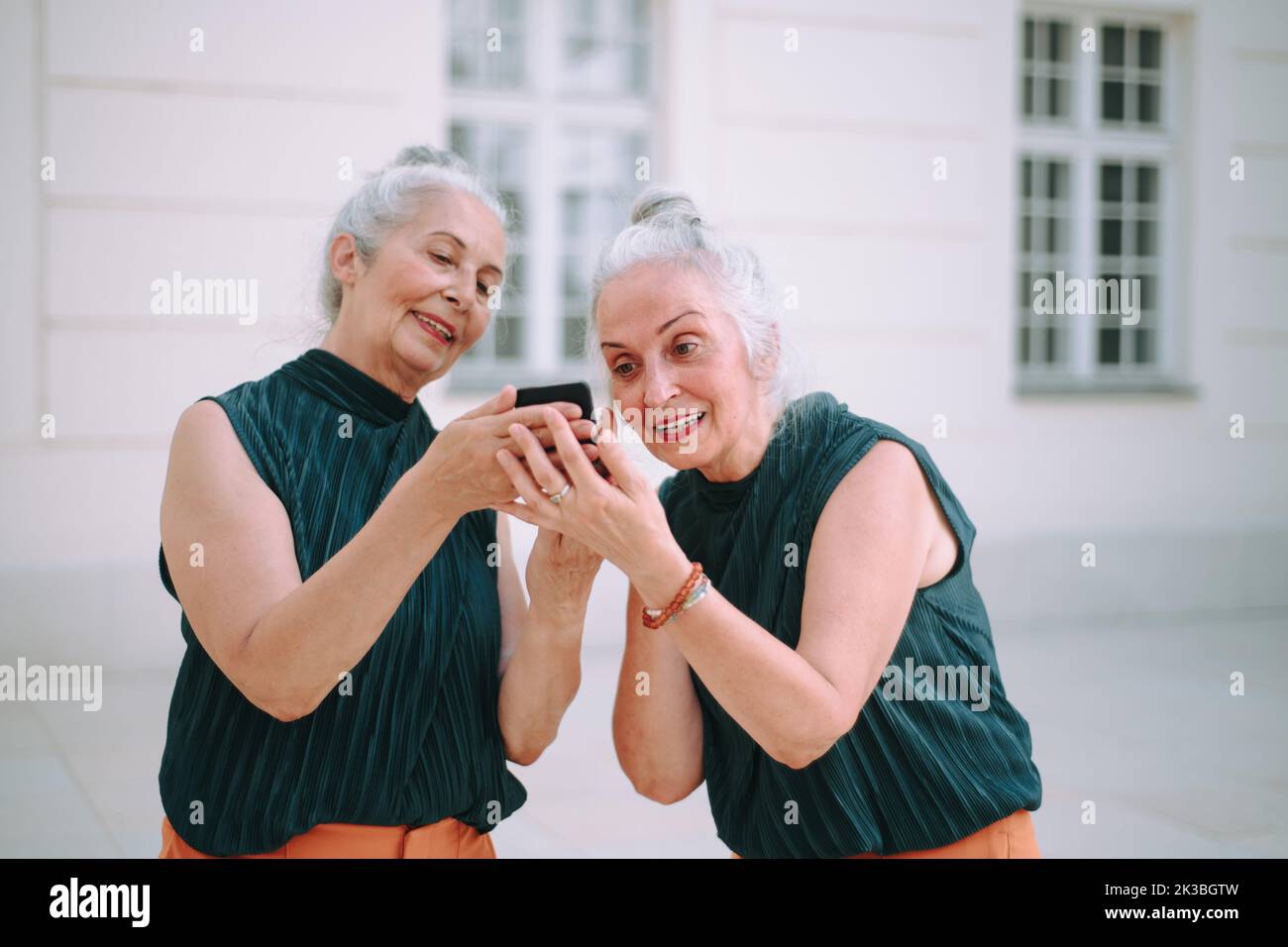 Donne anziane gemellano all'aperto in uno smartphone per il controllo della città. Foto Stock