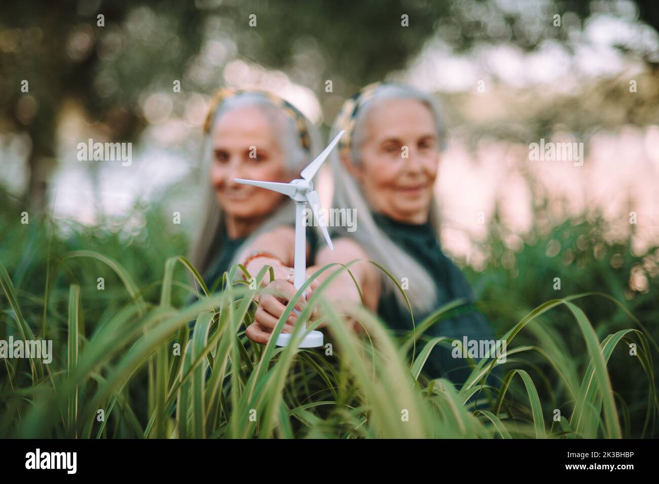 Donne anziane, gemelle che detengono il modello plastico della turbina eolica in natura, concetto di futuro, ecologia e risorse rinnovabili, messaggio per la prossima generazione. Foto Stock