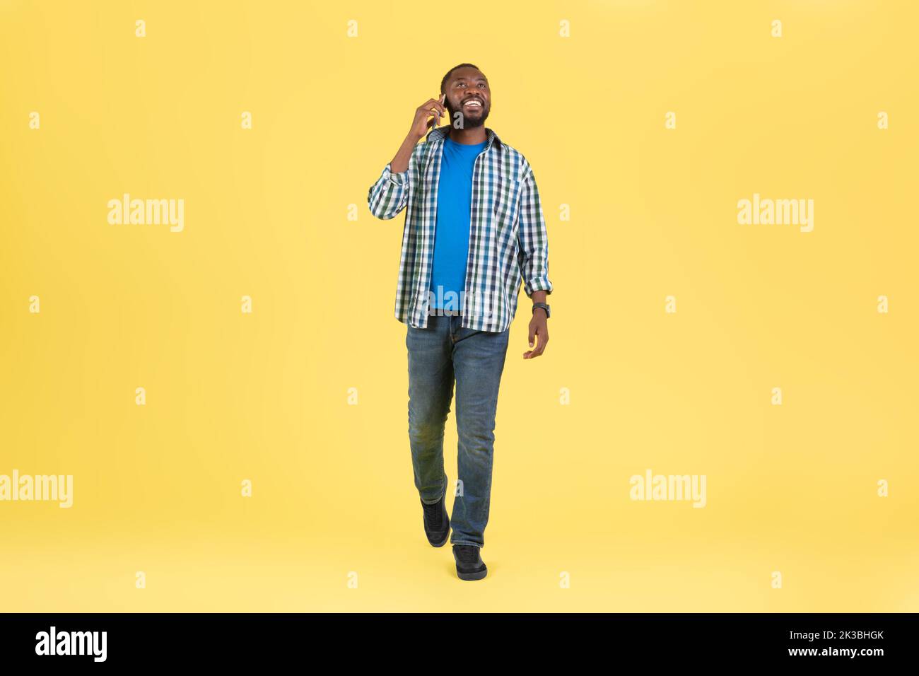 African Guy che parla al telefono comunicare camminando su sfondo giallo Foto Stock
