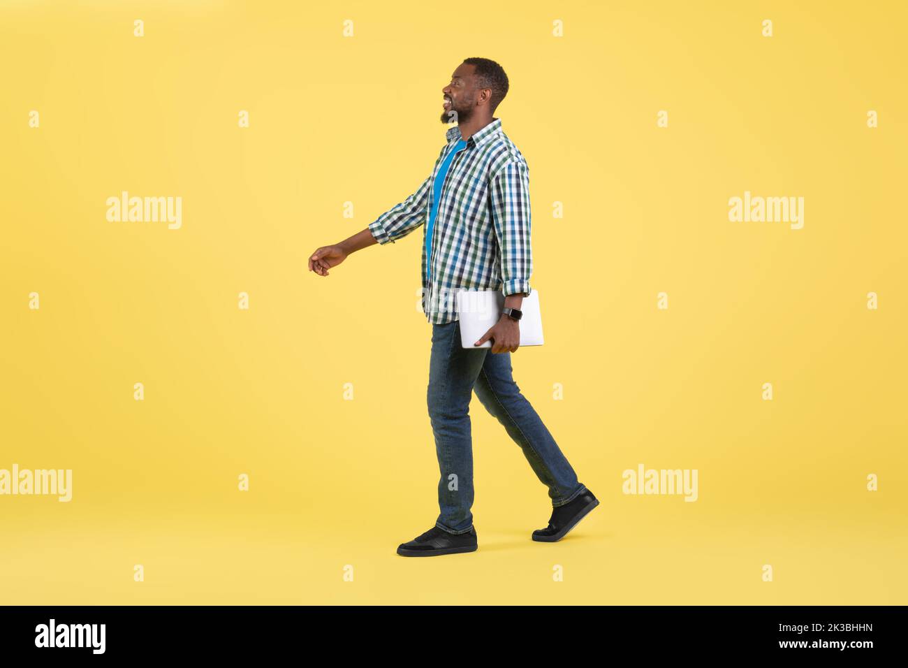 Happy Black Guy Holding laptop che cammina su sfondo giallo Foto Stock