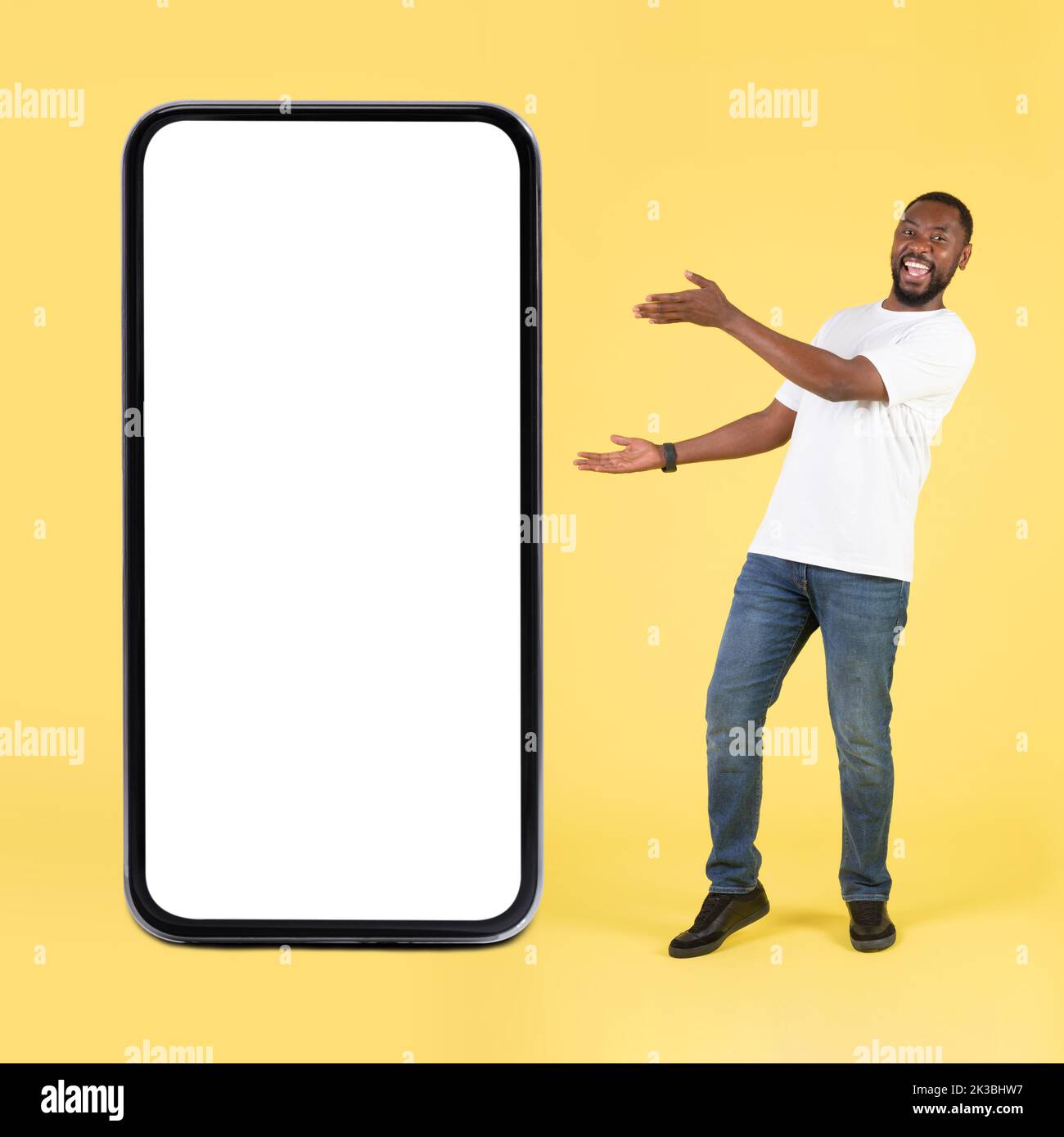 Gioioso ragazzo nero che mostra l'ampio schermo del telefono su sfondo giallo Foto Stock