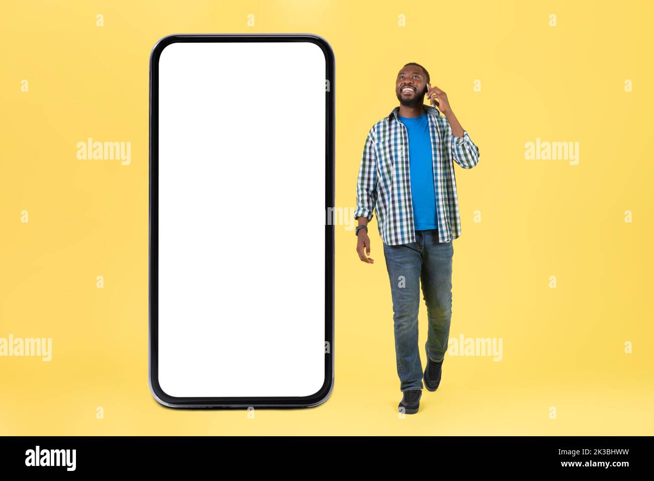 Black Guy parlando al telefono Walking vicino a grande cellulare, Studio Foto Stock