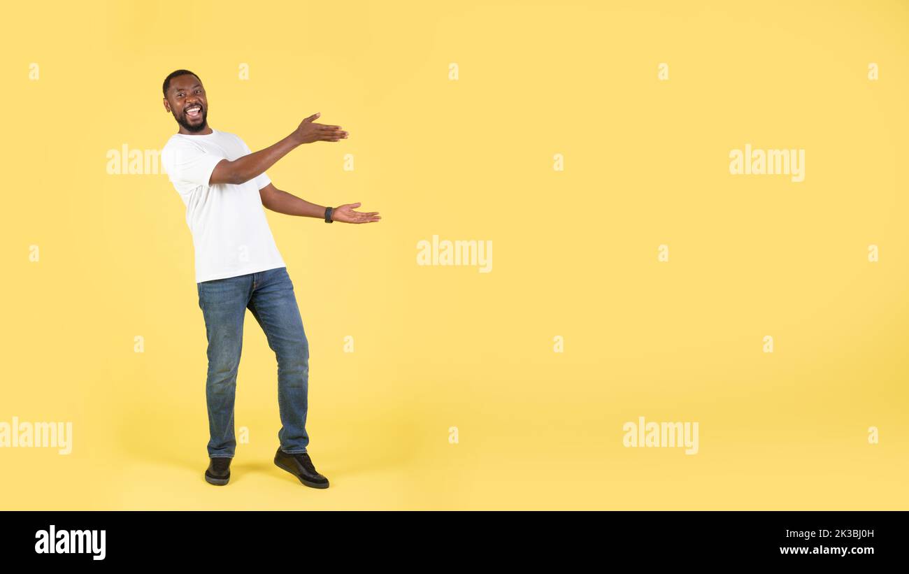 Maschio africano che mostra lo spazio vuoto con entrambe le mani, sfondo giallo Foto Stock