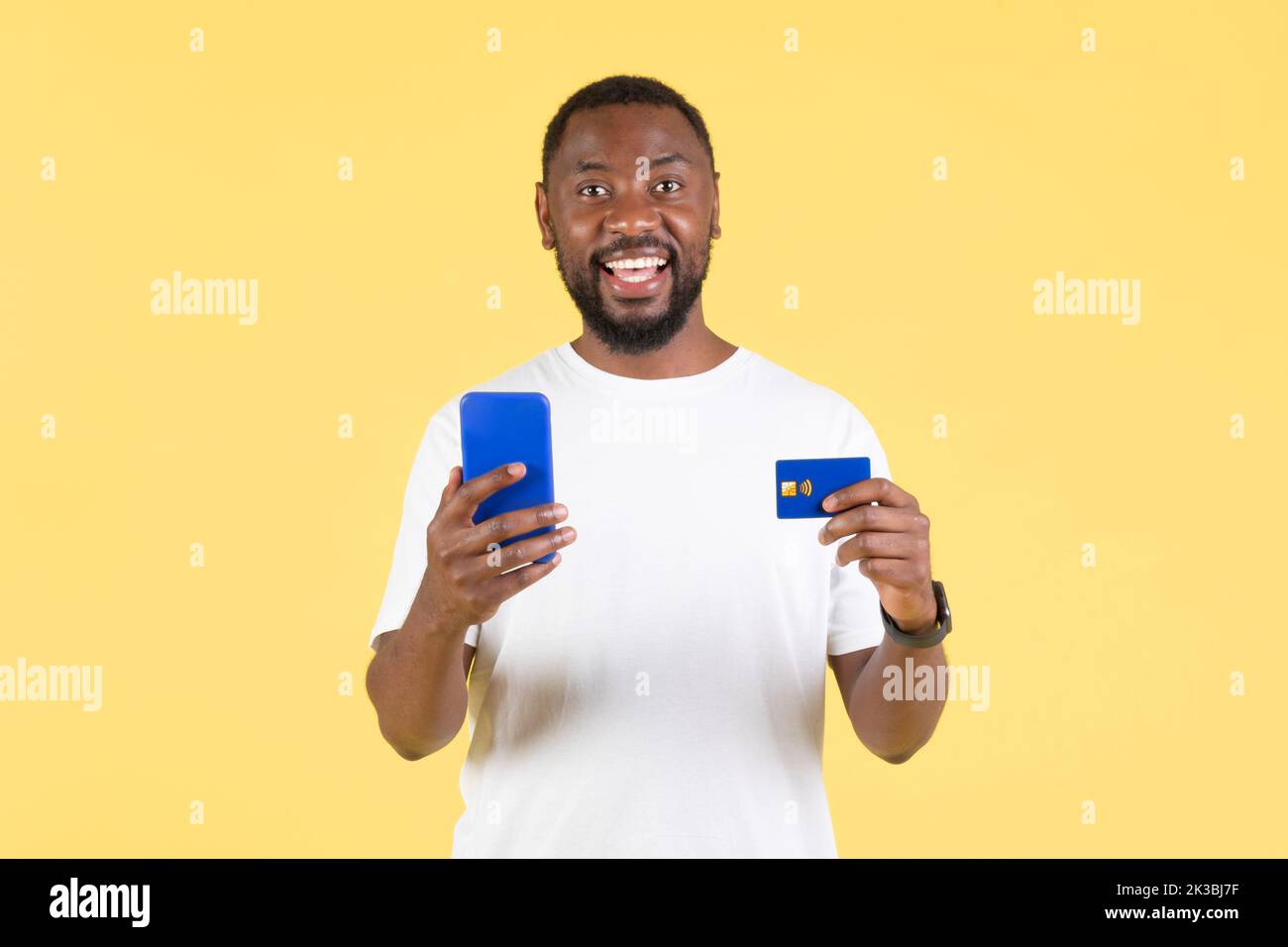 Black Man Shopping tramite smartphone e carta di credito, sfondo giallo Foto Stock