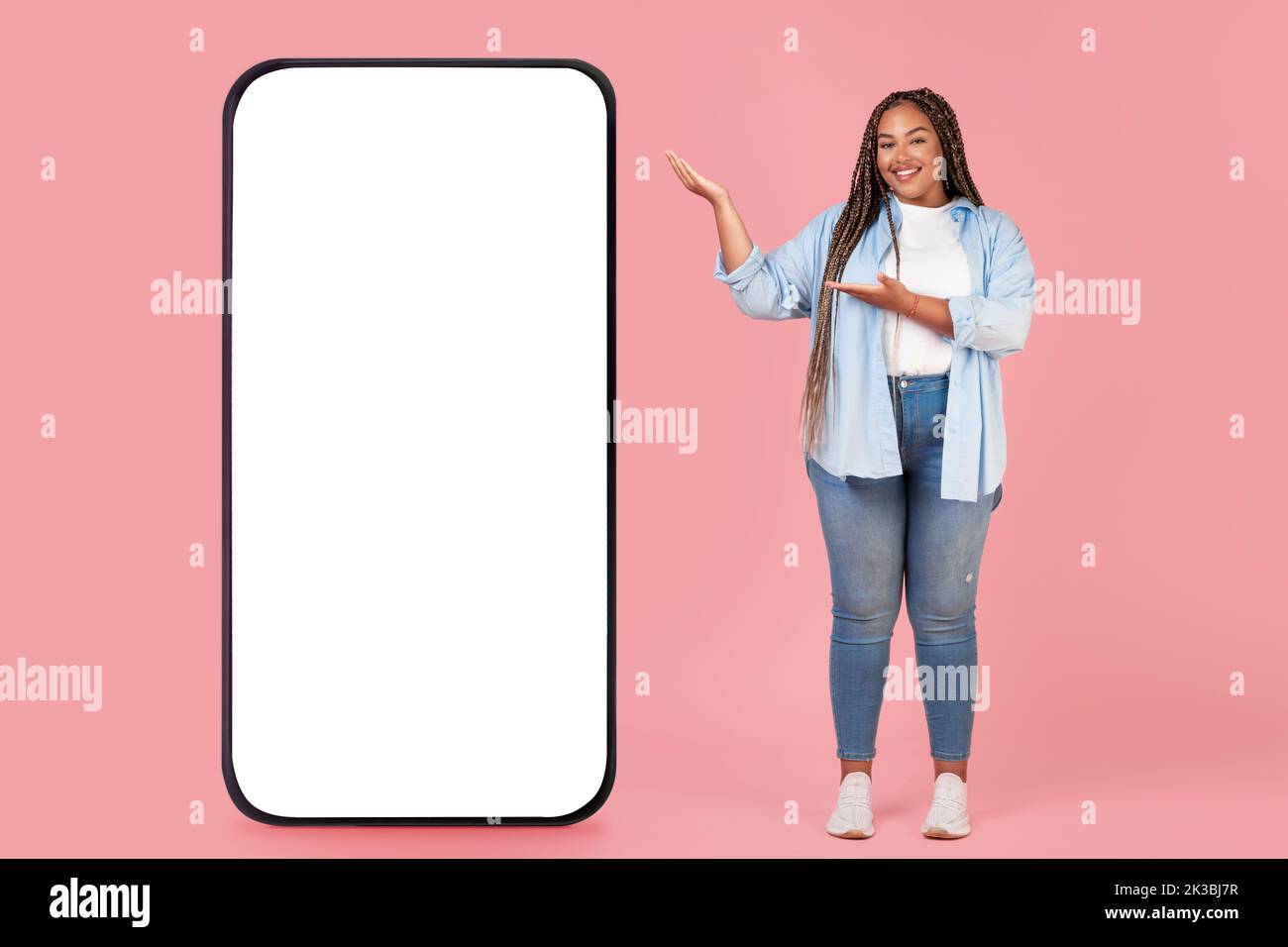 Black Lady mostra un enorme smartphone con schermo vuoto, sfondo rosa Foto Stock