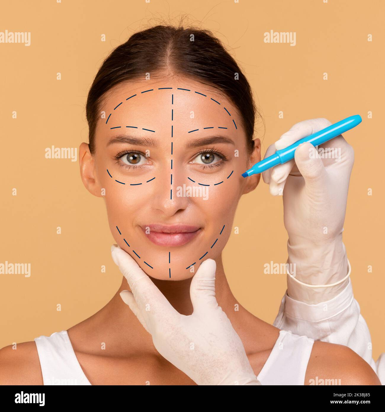 Il chirurgo di plastica che disegna i segni sul volto della giovane donna per l'operazione cosmetic dell'ambulatorio su sfondo beige dello studio Foto Stock
