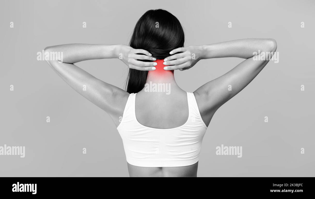 Vista posteriore della giovane donna che tocca la zona infiammata del collo, affetta da osteocondrosi cervicale Foto Stock
