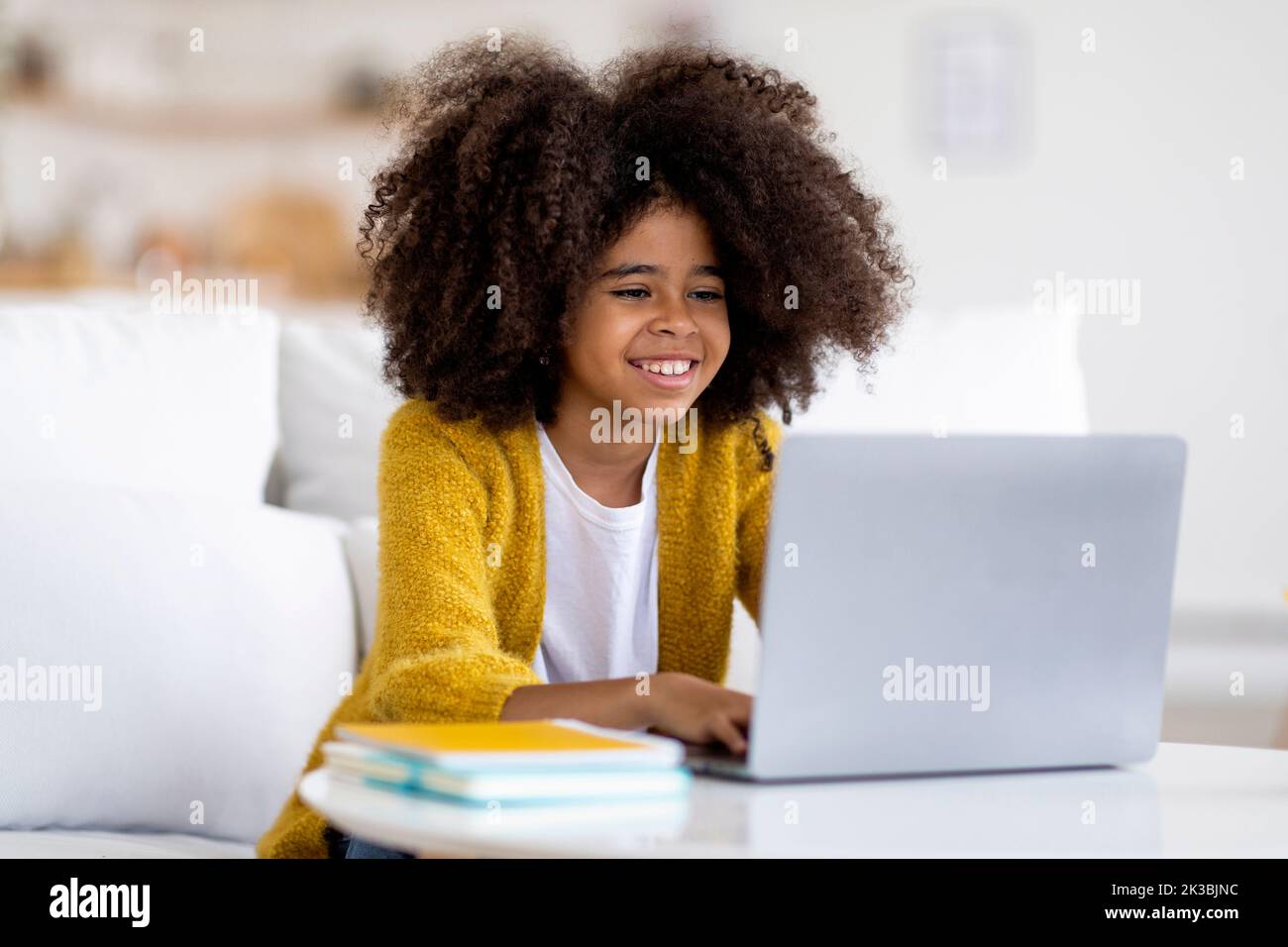 Allegro ragazza nera scolaro facendo i compiti a casa, utilizzando il computer Foto Stock