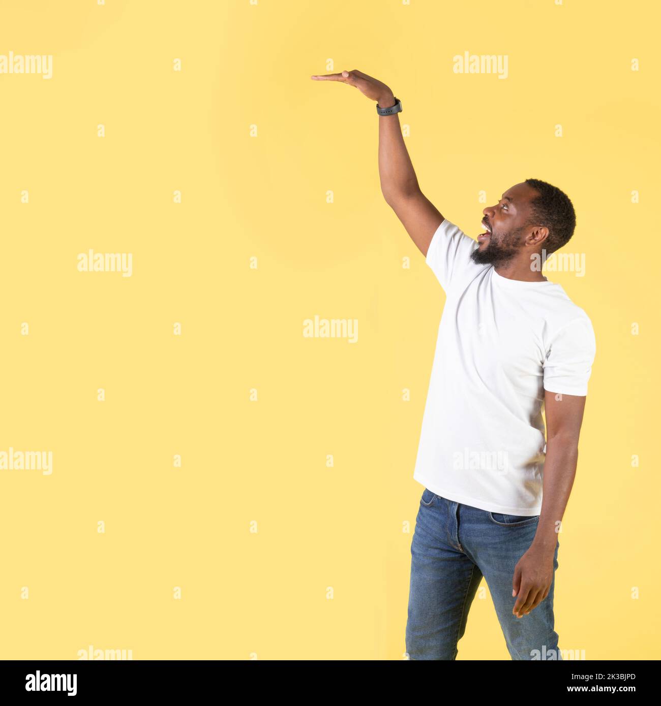 Uomo Africano che alza il braccio che misura e mostra l'altezza, sfondo giallo Foto Stock