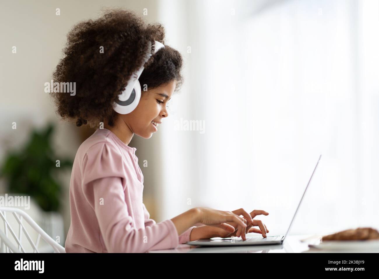 Vista laterale della bambina nera che digita sulla tastiera del computer portatile Foto Stock