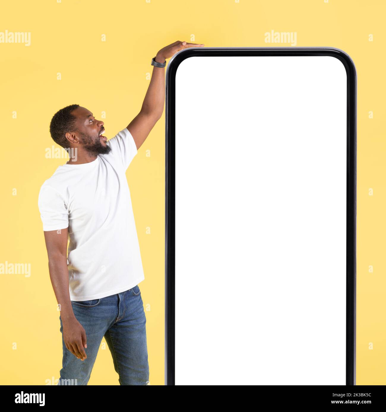 Uomo afroamericano che tocca il telefono grande in piedi su sfondo giallo Foto Stock