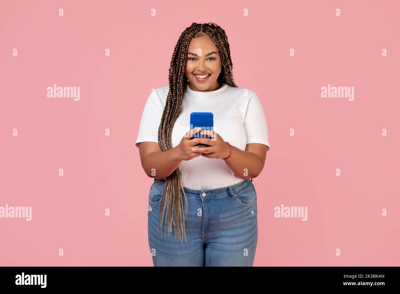 Happy Black Lady utilizzando il telefono texting in piedi su sfondo rosa Foto Stock