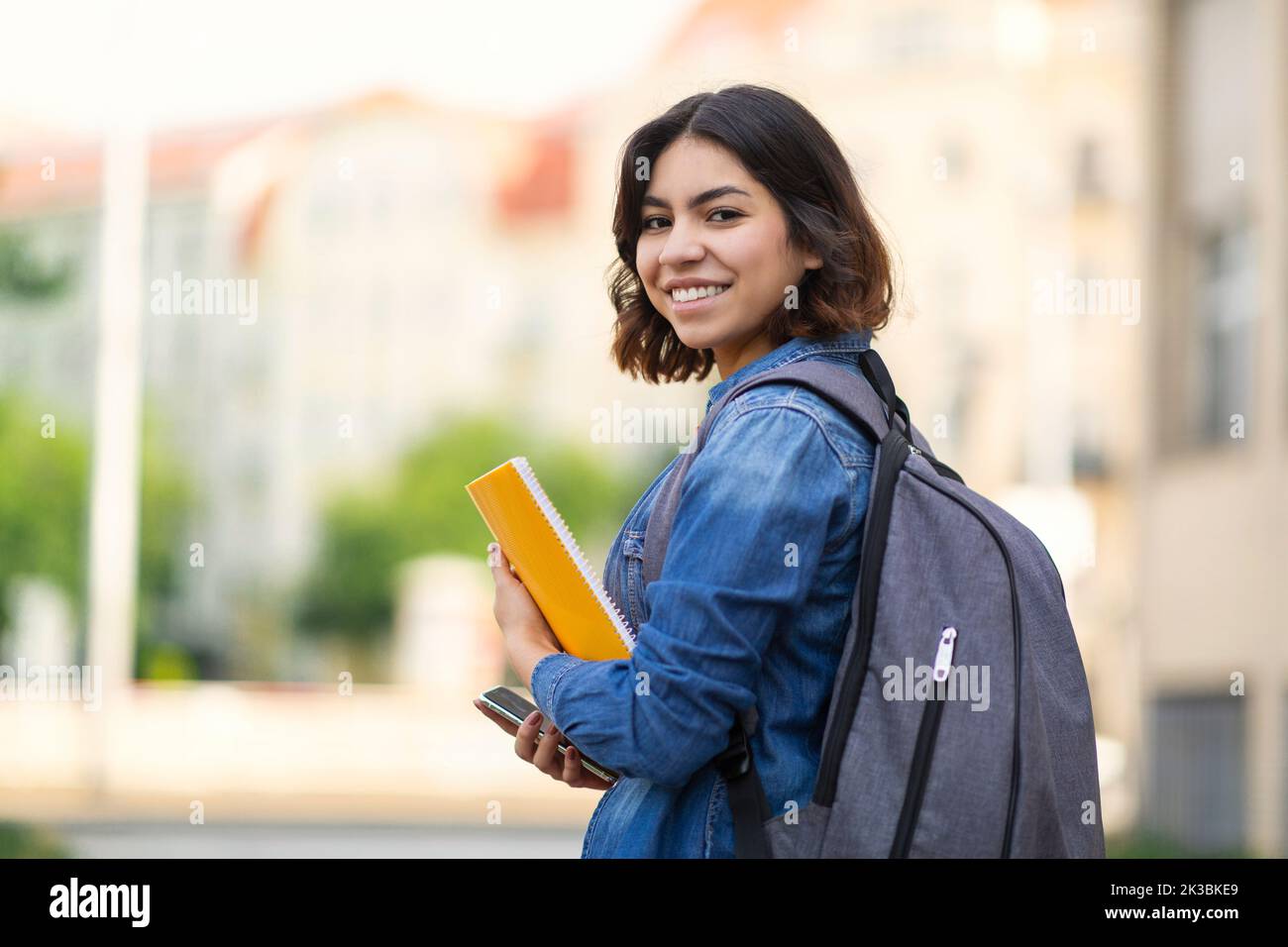 Giovane studentessa araba sorridente con libri da lavoro e zaino in piedi all'aperto Foto Stock