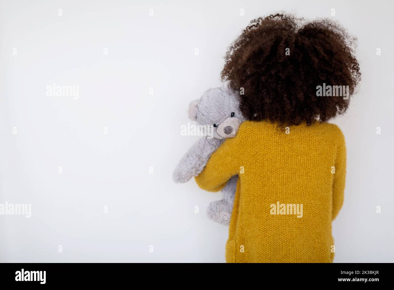 Vista posteriore del bambino nero che tiene orsacchiotto, sfondo bianco Foto Stock