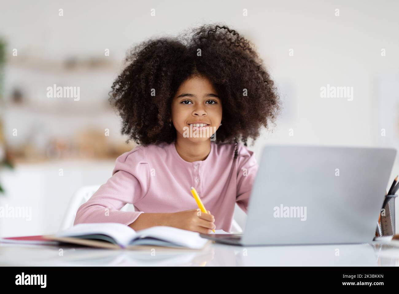 Piccola ragazza nera graziosa che fa i compiti a casa, usando il calcolatore Foto Stock