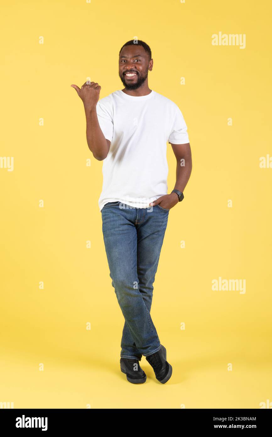 Vertical Shot of Cheerful Black Guy che punta il pollice da parte, Studio Foto Stock
