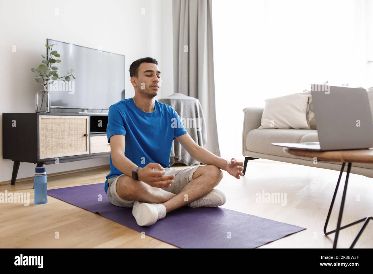 Concetto di meditazione del mattino. Ragazzo arabo che pratica yoga, meditando con gli occhi chiusi davanti al computer portatile, spazio copia Foto Stock