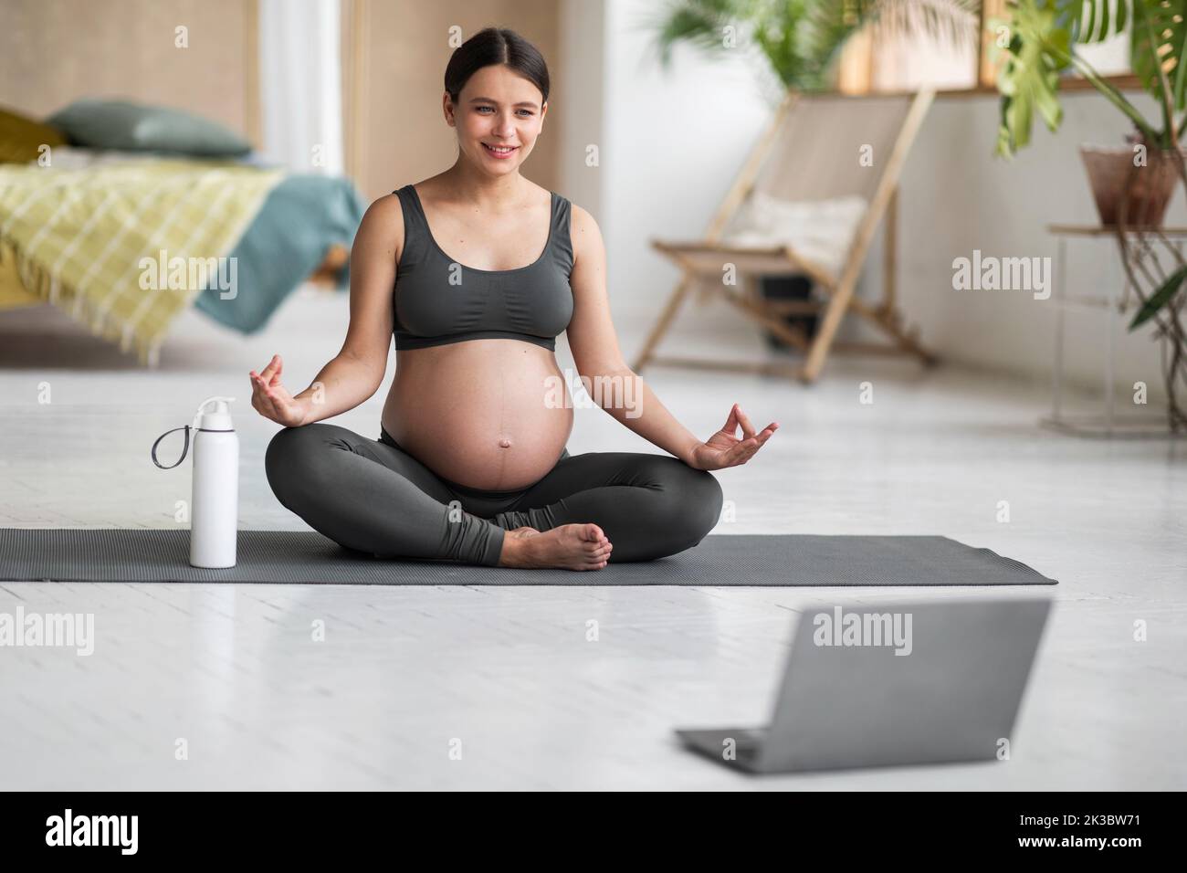 Donna incinta sorridente con il laptop che pratica lo yoga in linea a casa Foto Stock