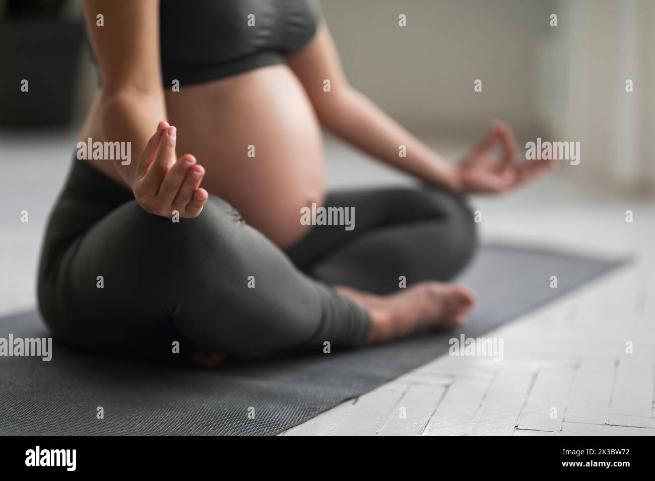 Primo piano colpo di donna incinta irriconoscibile meditare in posizione Lotus a casa Foto Stock