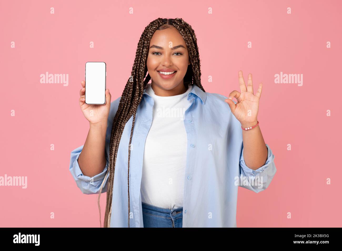 Donna Africana americana che mostra lo schermo del telefono gesturing okay, sfondo rosa Foto Stock