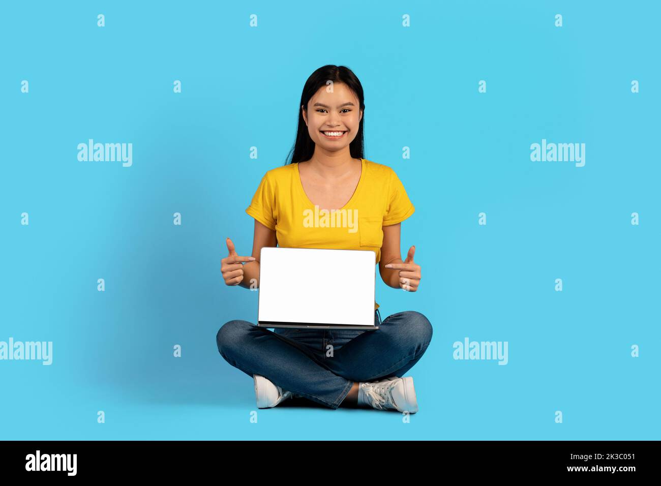 Raccomandazioni e consigli per lo studio. Sorridente giovane studentessa coreana siede in posizione lotus Foto Stock