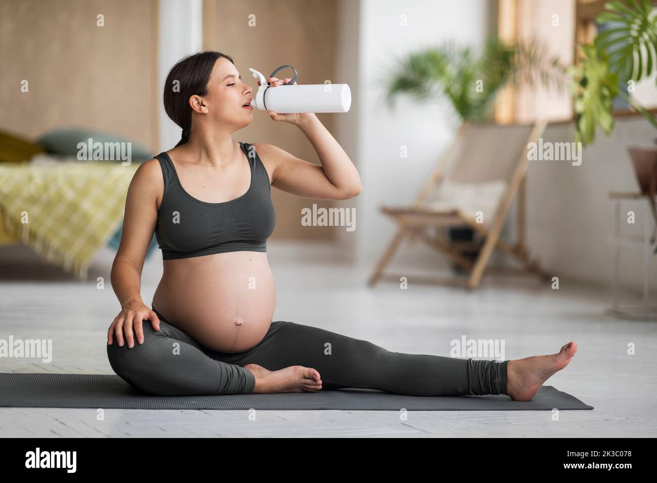 Giovane donna incinta bere acqua dalla bottiglia durante l'allenamento di yoga a casa Foto Stock