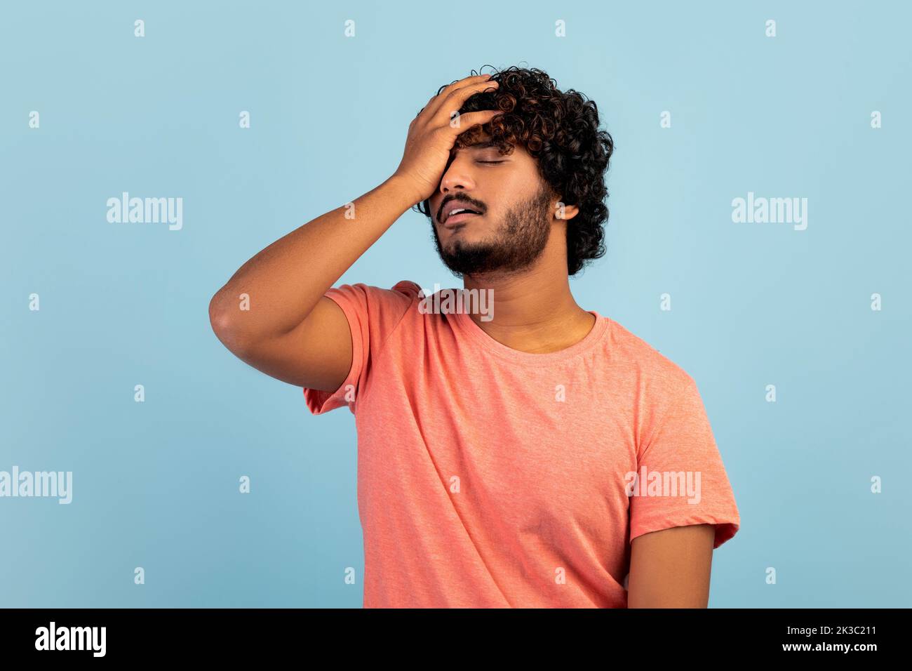 Triste ragazzo orientale che tocca la testa, sfondo blu Foto Stock