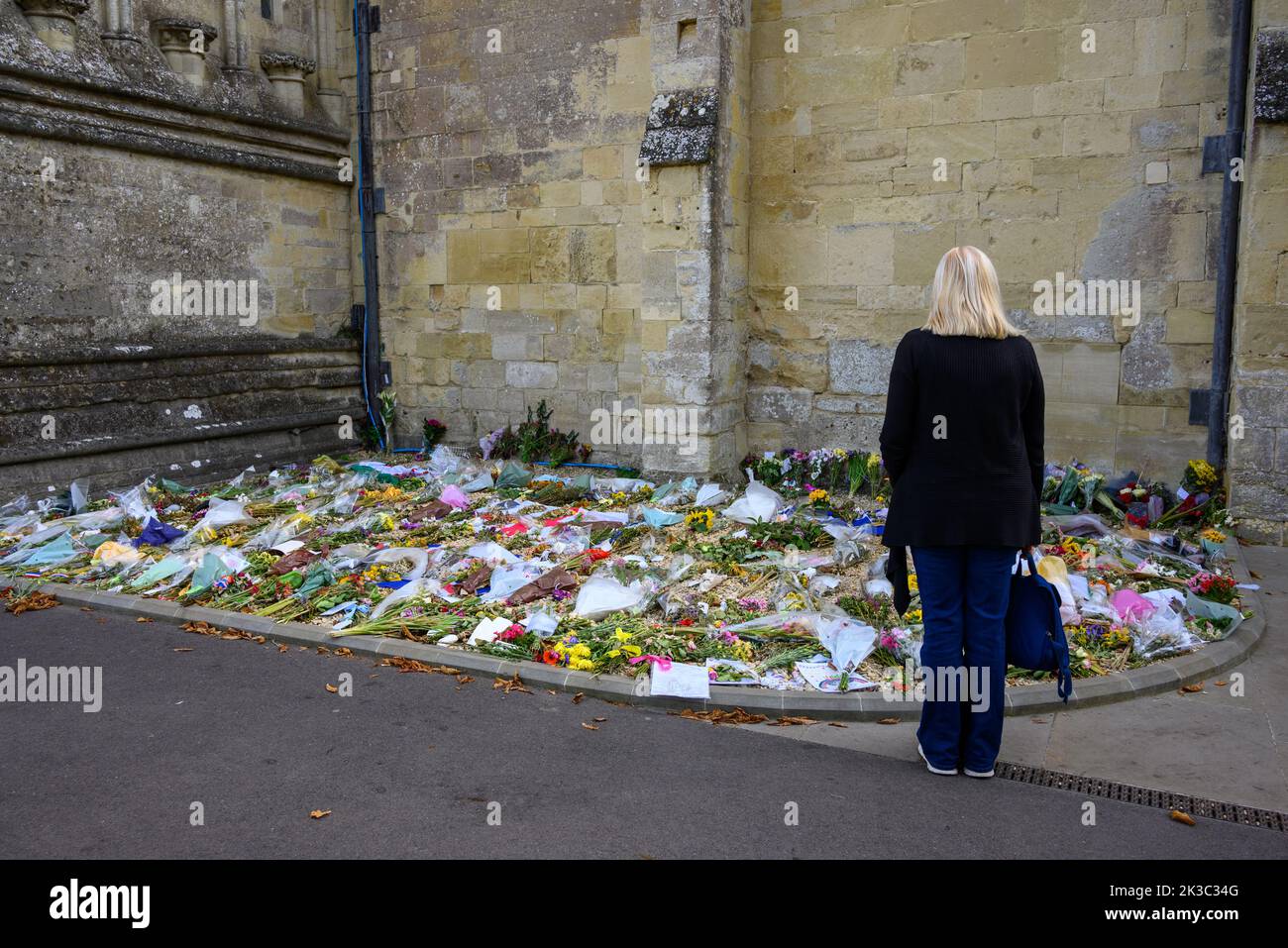 Donna che guarda i fiori deposti in tributo alla morte della defunto Regina Elisabetta II fuori dalla cattedrale di Salisbury, nel Wiltshire, Regno Unito Foto Stock