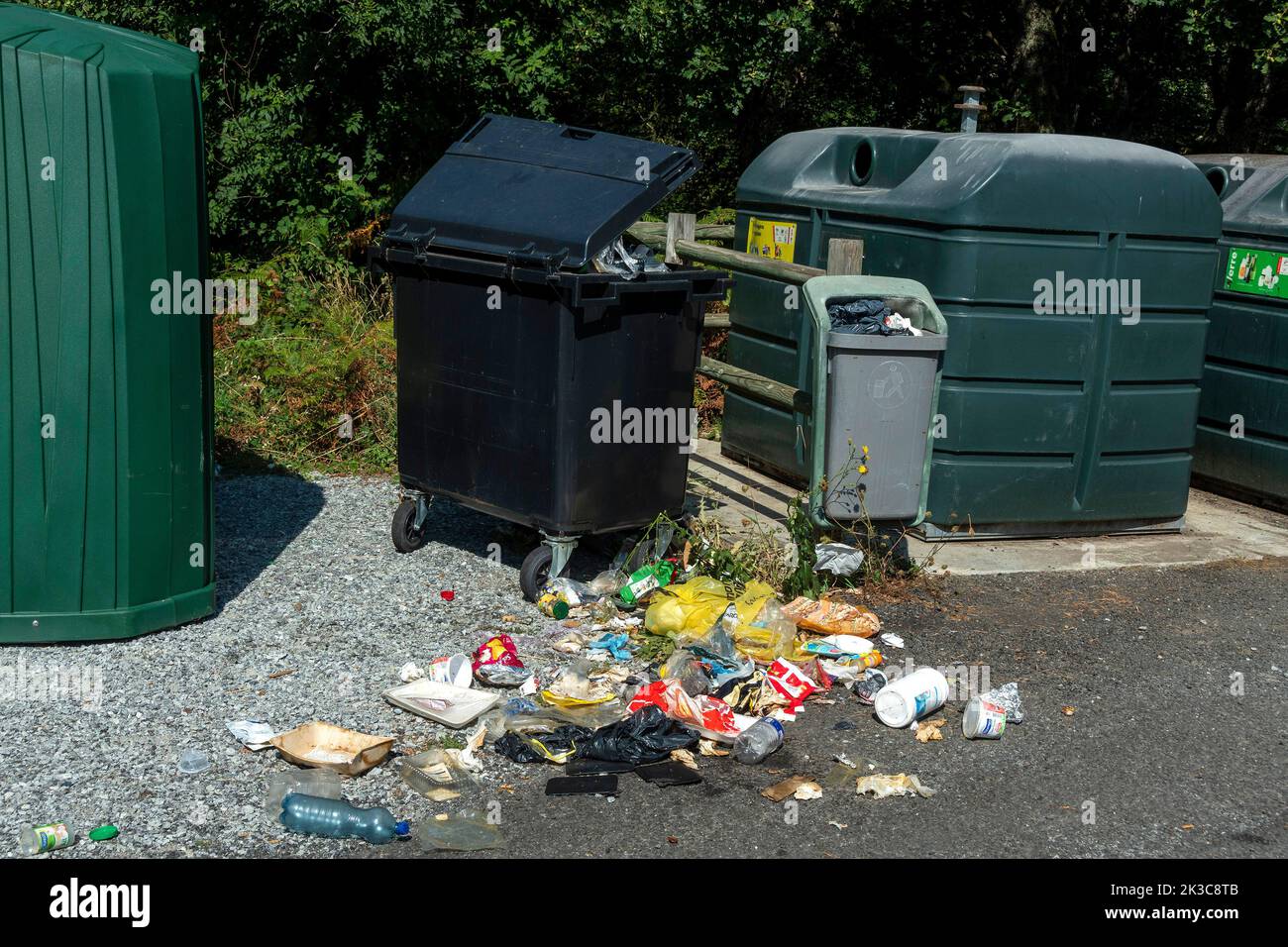 Cestino traboccante con rifiuti sparsi accanto ai contenitori di riciclaggio in un'area pubblica Foto Stock