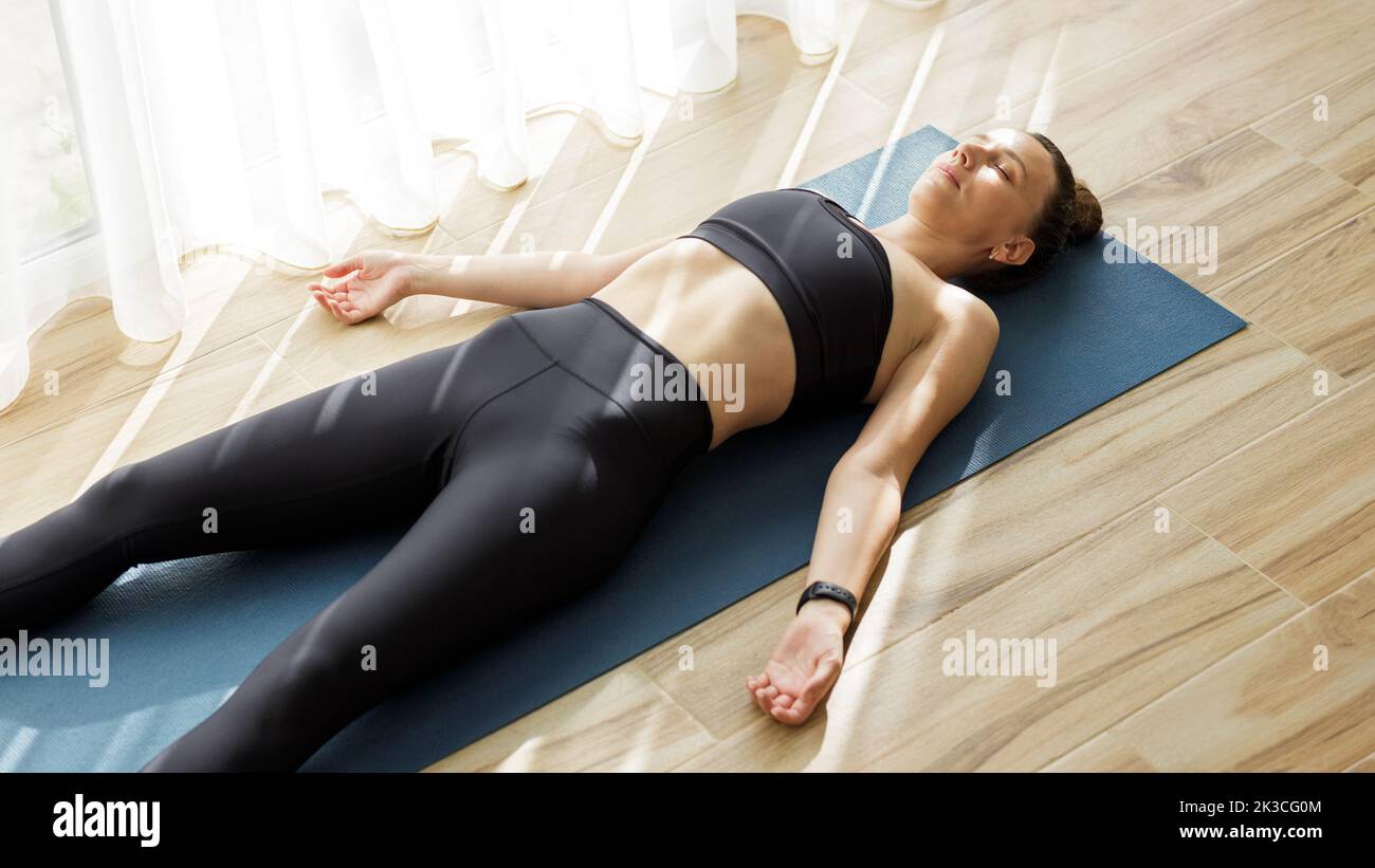 Giovane donna che si rilassa in shavasana o in corpse yoga posa dopo il suo allenamento mattutino Foto Stock