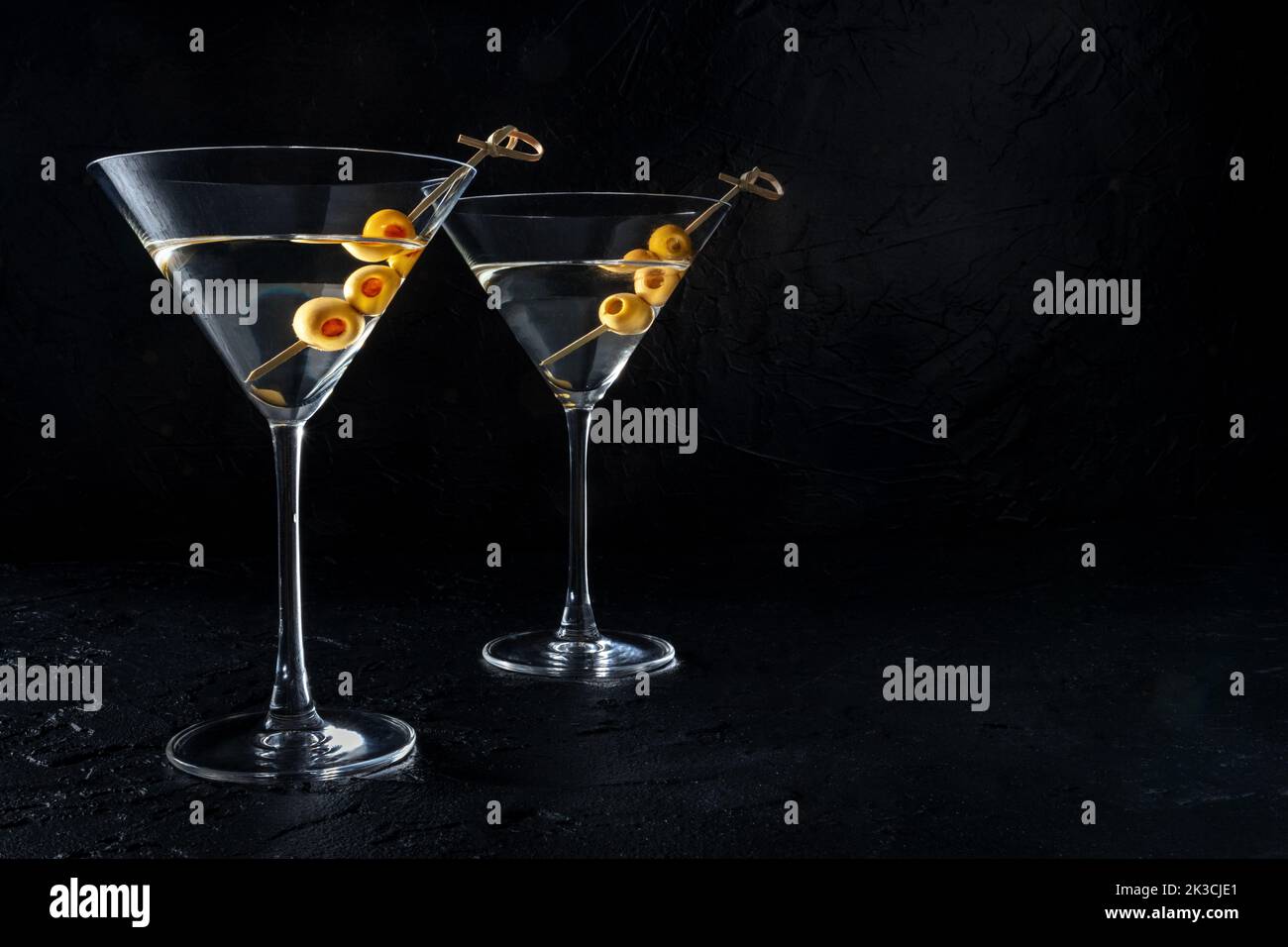 Martini, due bicchieri con olive speziate, su fondo nero. Bevande alcoliche con un posto per il testo Foto Stock