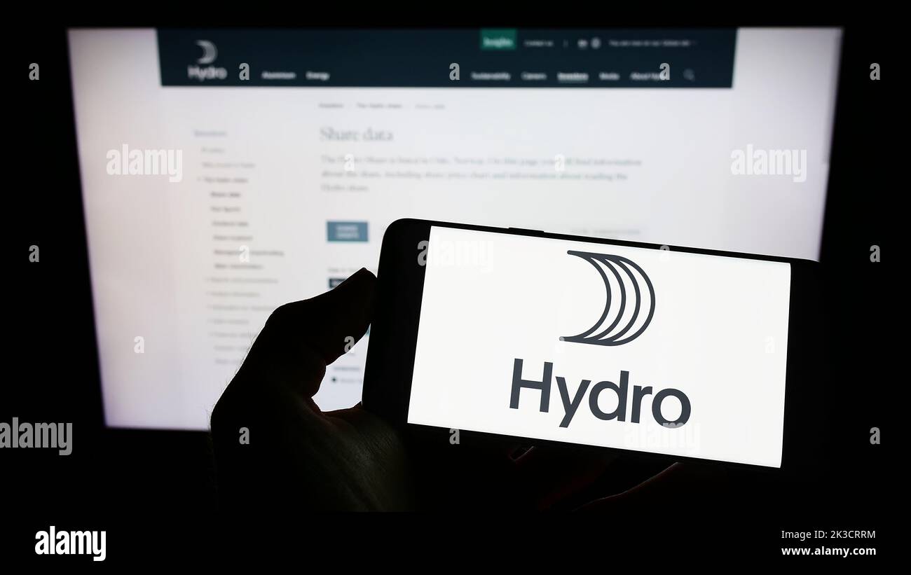 Persona che tiene uno smartphone con il logo della società norvegese di alluminio Norsk Hydro ASA sullo schermo di fronte al sito Web. Messa a fuoco sul display del telefono. Foto Stock