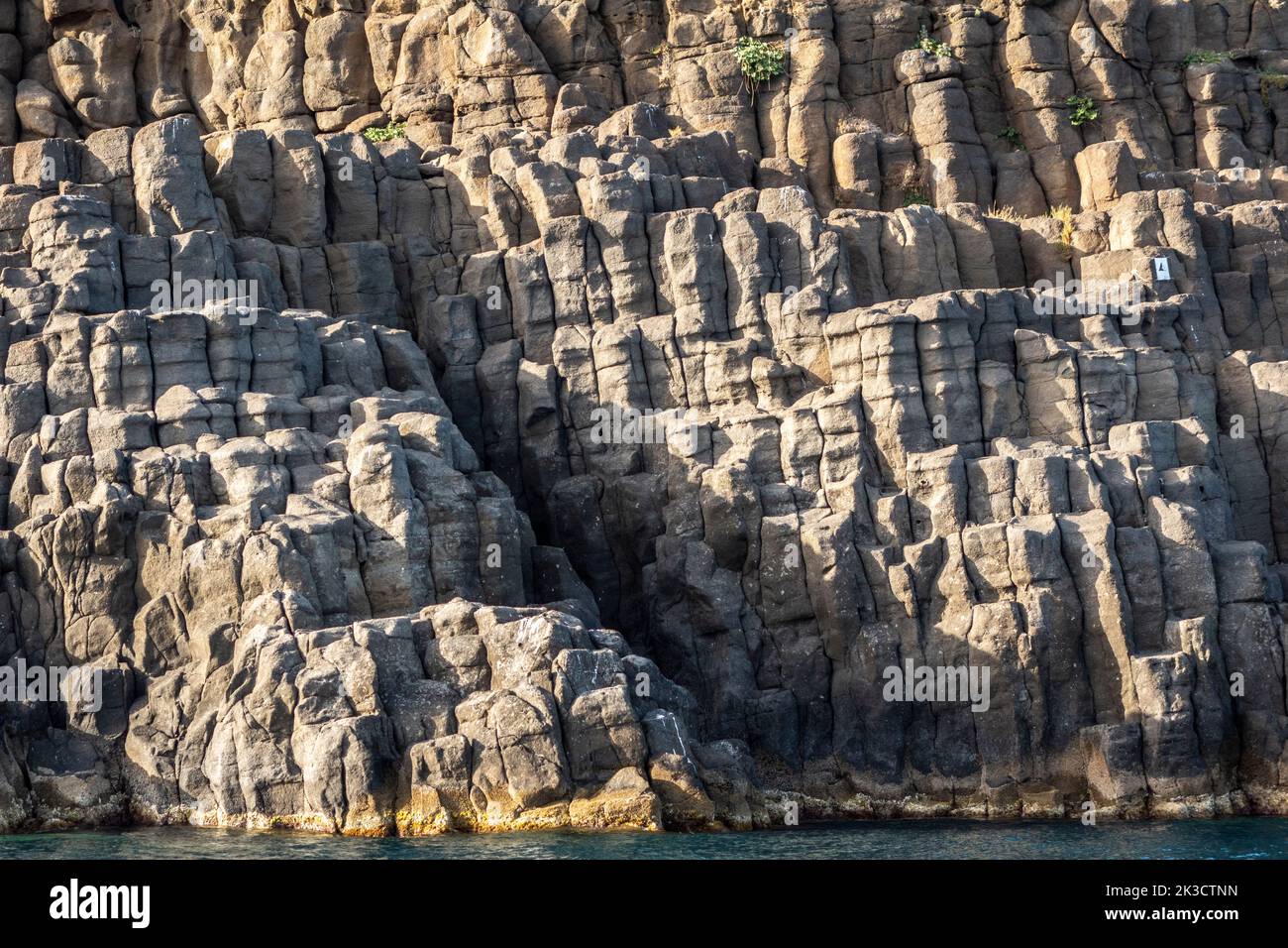 Formazioni rocciose colonnari basaltiche sul Faraglione Grande, uno dei Faraglioni (Isole dei Ciclopi), un gruppo di cataste di mare vulcaniche ad Aci Trezza, in Sicilia Foto Stock