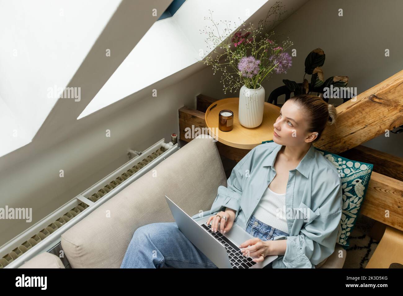 Vista ad angolo alto della donna che guarda la finestra mentre usa il notebook sul divano a casa, immagine di scorta Foto Stock