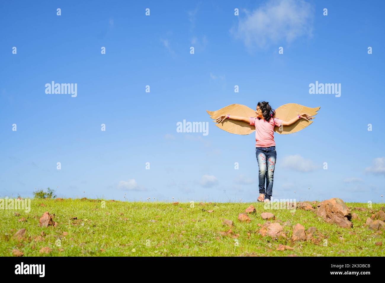 ragazza felice eccitato capretto con ali artificiali che ballano come un uccello sulla collina in prato verde contro cielo blu - concetto di libertà, happines e. Foto Stock