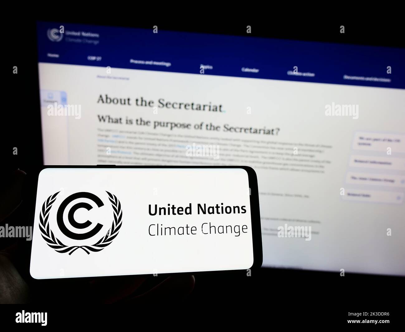 Persona che tiene in mano uno smartphone con il logo del trattato delle Nazioni Unite sull'ambiente UNFCCC sullo schermo di fronte al sito Web. Messa a fuoco sul display del telefono. Foto Stock