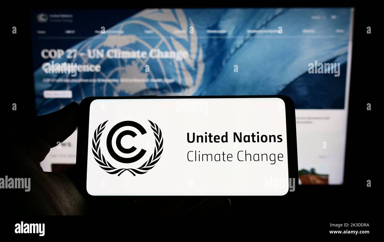 Persona che tiene il telefono cellulare con il logo del trattato ambientale delle Nazioni Unite UNFCCC sullo schermo di fronte alla pagina web. Messa a fuoco sul display del telefono. Foto Stock