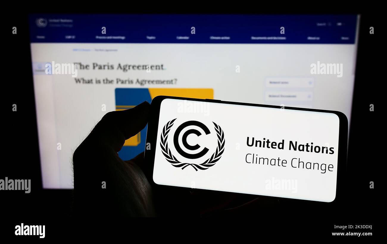 Persona che tiene il cellulare con il logo del trattato ambientale delle Nazioni Unite UNFCCC sullo schermo di fronte alla pagina web. Messa a fuoco sul display del telefono. Foto Stock