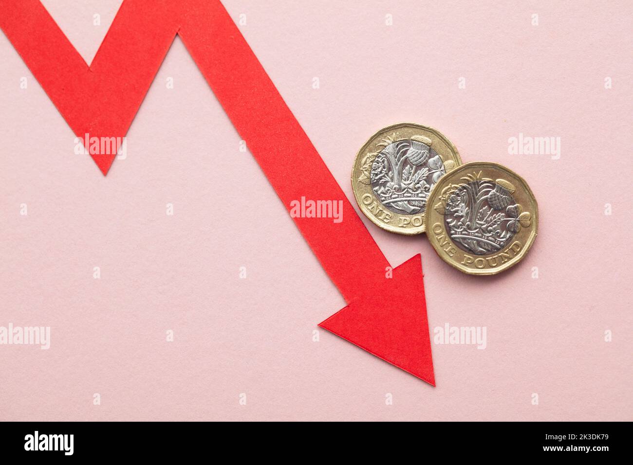 Monete in sterline britanniche con una freccia rossa rivolta verso il basso. Crisi economica del Regno Unito Foto Stock