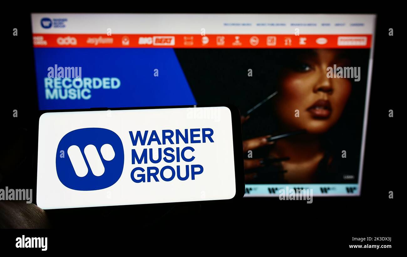 Persona che tiene il cellulare con il logo della società di intrattenimento Warner Music Group Corp. Sullo schermo di fronte alla pagina web. Messa a fuoco sul display del telefono. Foto Stock