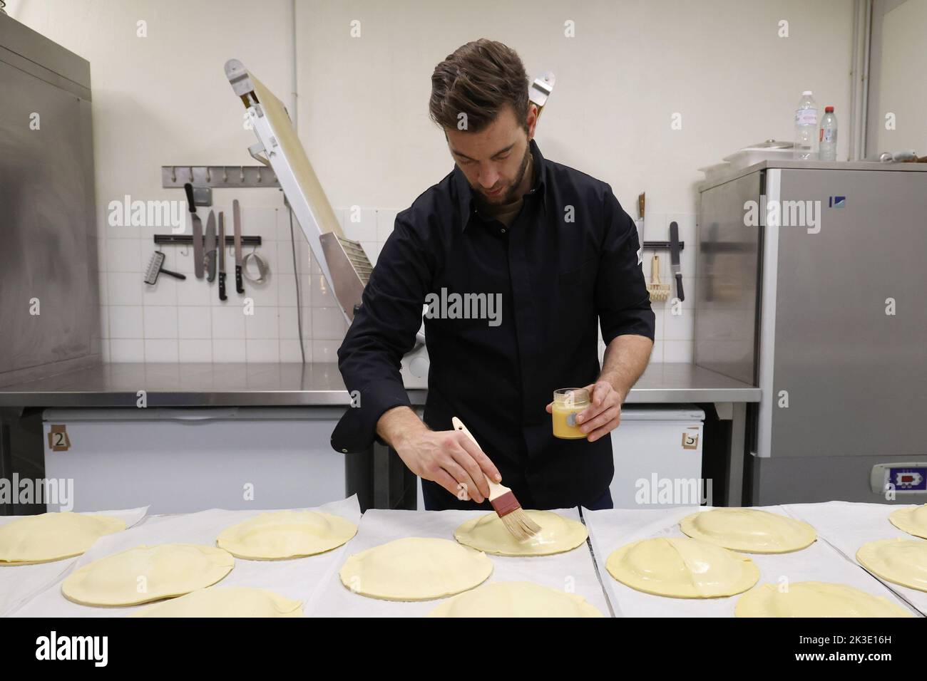 La Turbie, 5 gennaio 2022: Pasticciere che prepara una torta frangipane “galette des roi”, spazzolando l’esterno della pasta sfoglia con un uovo di gallina Foto Stock