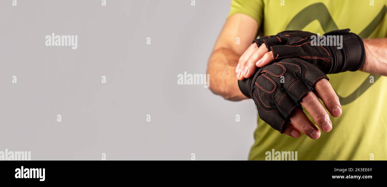 Guanti sportivi da allenamento, vestirsi a mani maschili per allenarsi in palestra. Banner pubblicitario con spazio di copia per il testo. Foto Stock