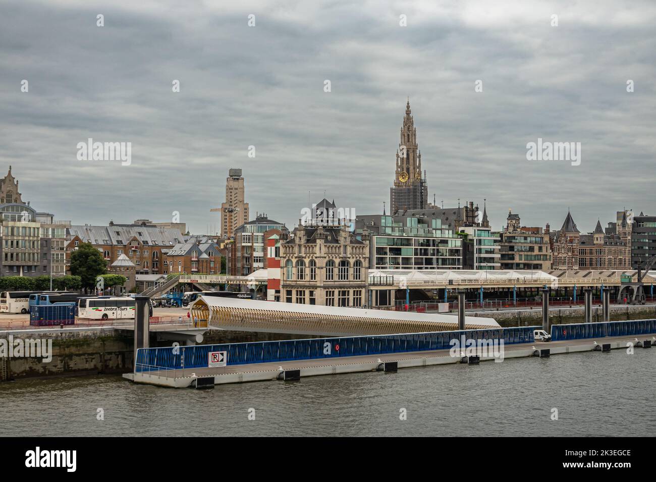 Anversa, Fiandre, Belgio - 10 luglio 2022: Industria lungo il fiume Scheldt. Skyline della città dietro il ponton di sbarco ormeggiato al molo sotto la fitta nuvola Foto Stock