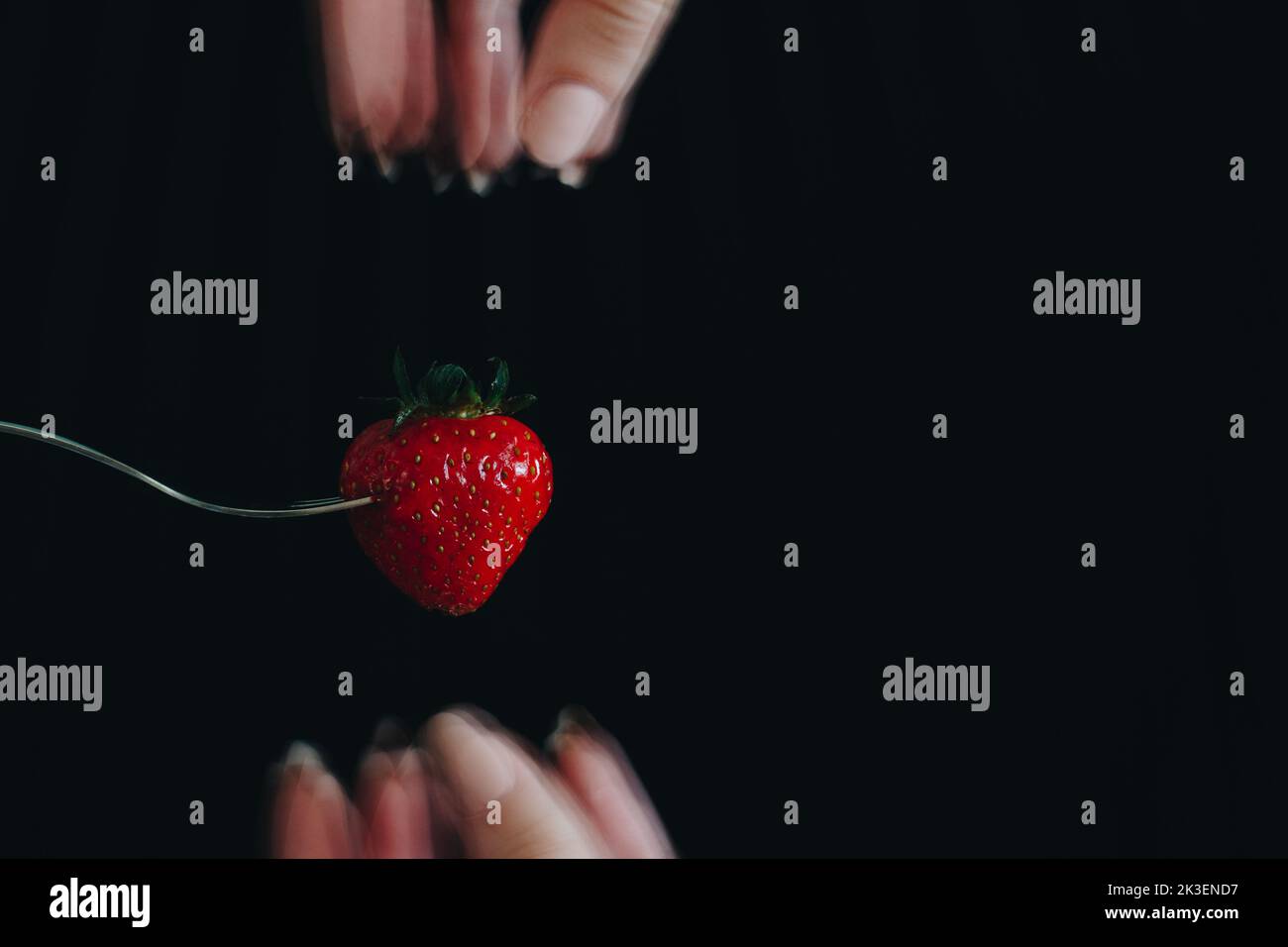 fragola bloccata in una forchetta su uno sfondo nero. Le dita della donna sono sfocate. Studio fotografico. Su misura per le campagne pubblicitarie. Foto Stock