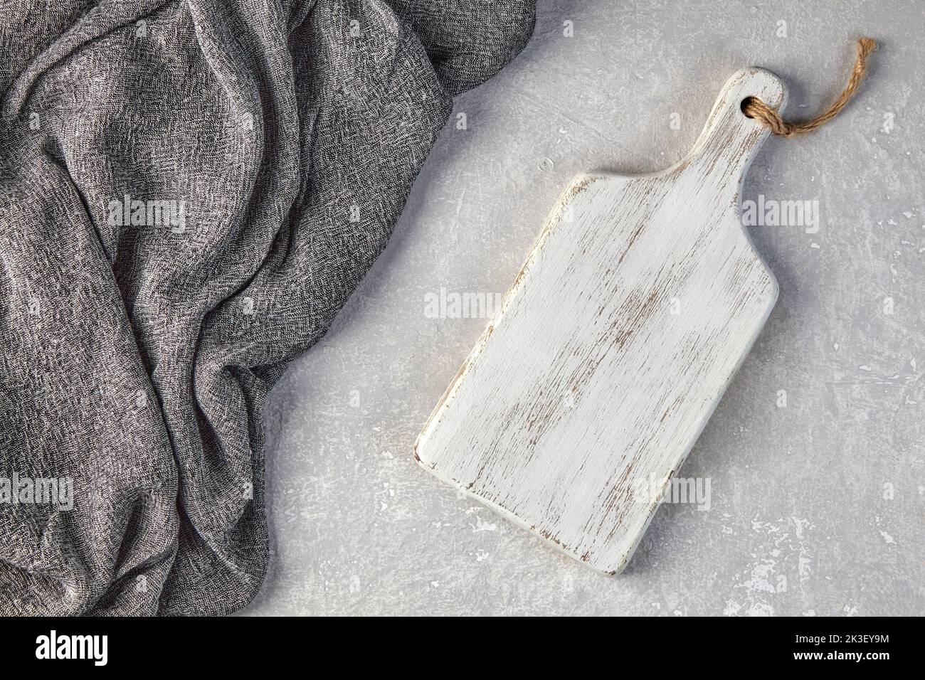 Camera di taglio in legno bianco e asciugamano da cucina grigio su un tavolo in cemento grigio chiaro Foto Stock