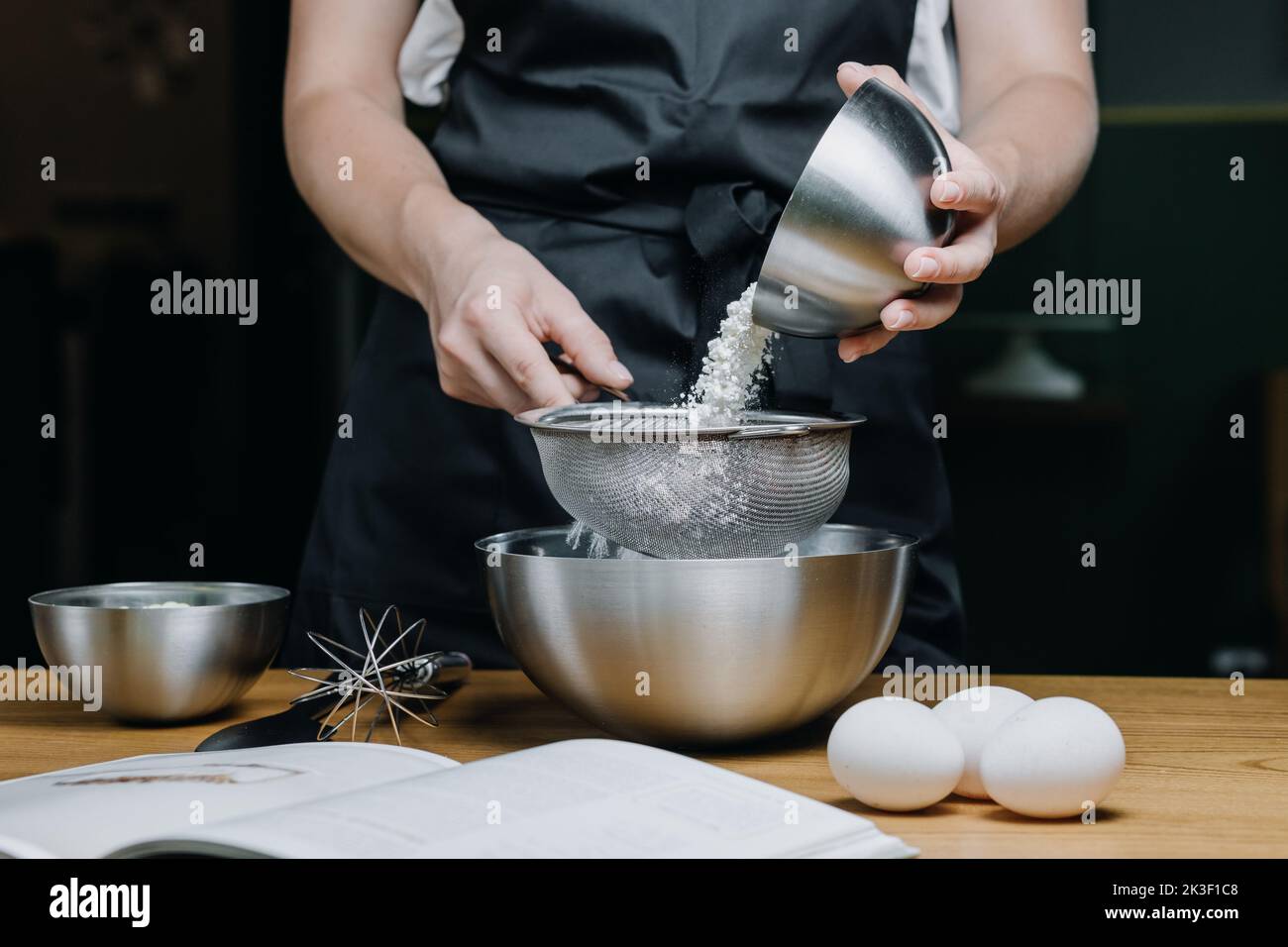 Le giovani mani femminili versano la farina da un piatto in un primo piano del setaccio Foto Stock